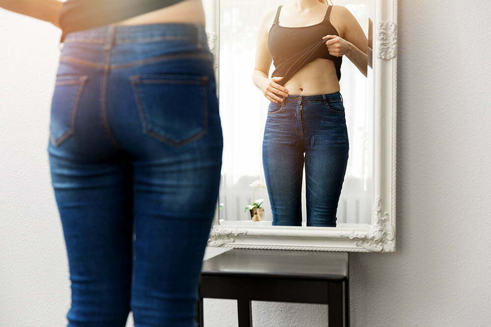 woman looking at tummy in mirror