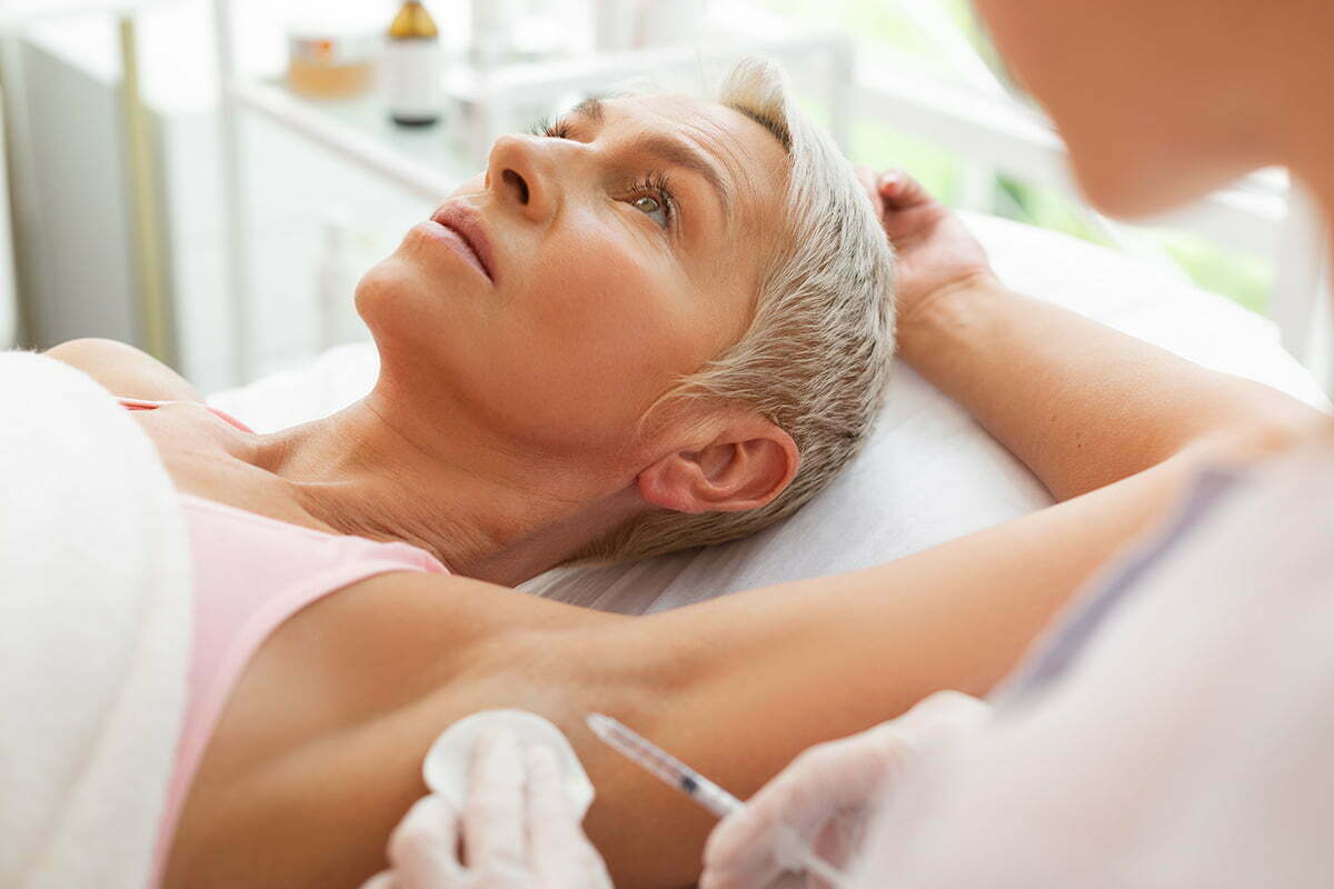 reclined woman presents armpit for botox injection from doctor